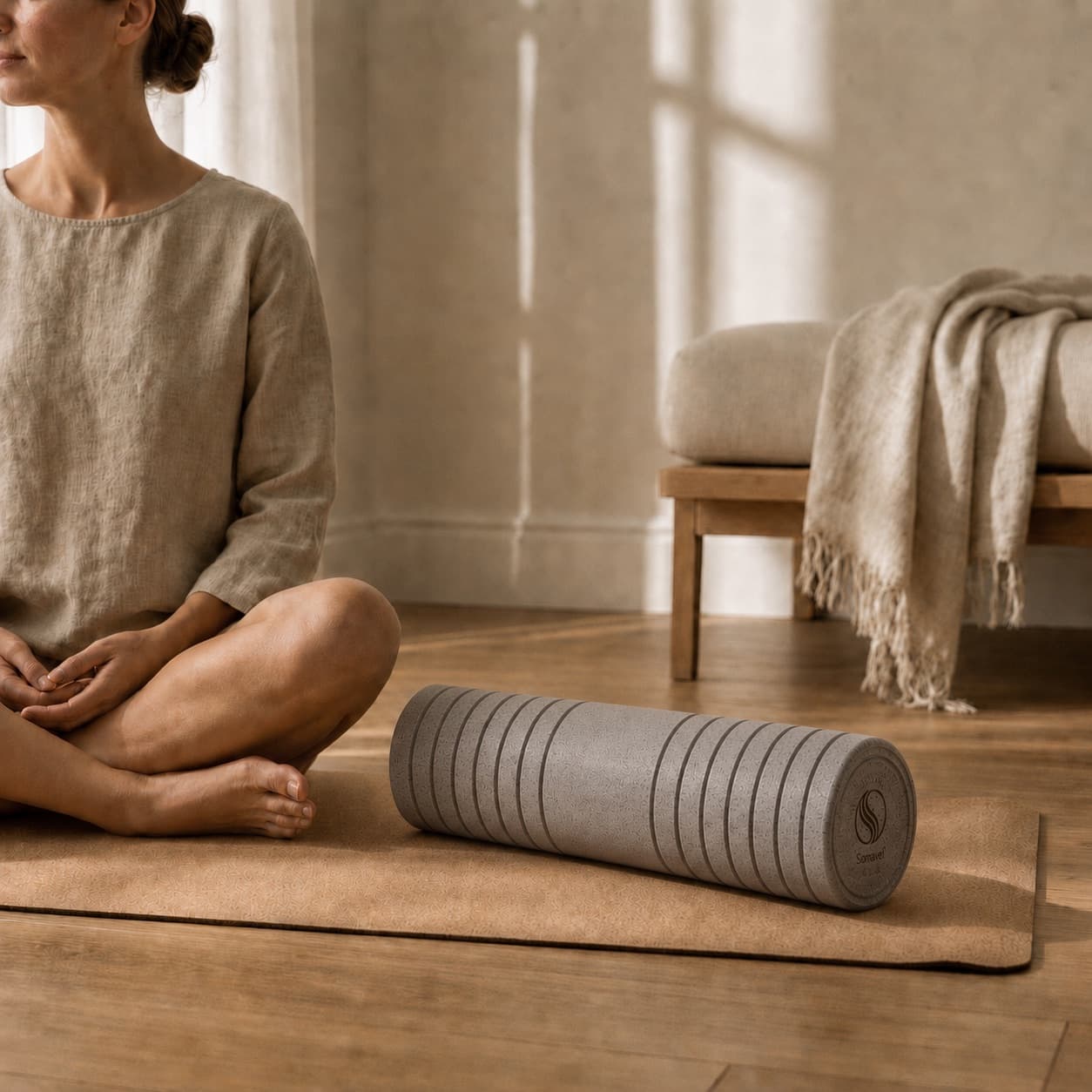 A woman seated beside the Sōmavel cork roller on the mat in a calm, sunlit room